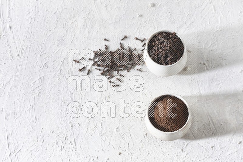 2 Beige ceramic bowls, one full of cloves and the other full of powder on textured white flooring