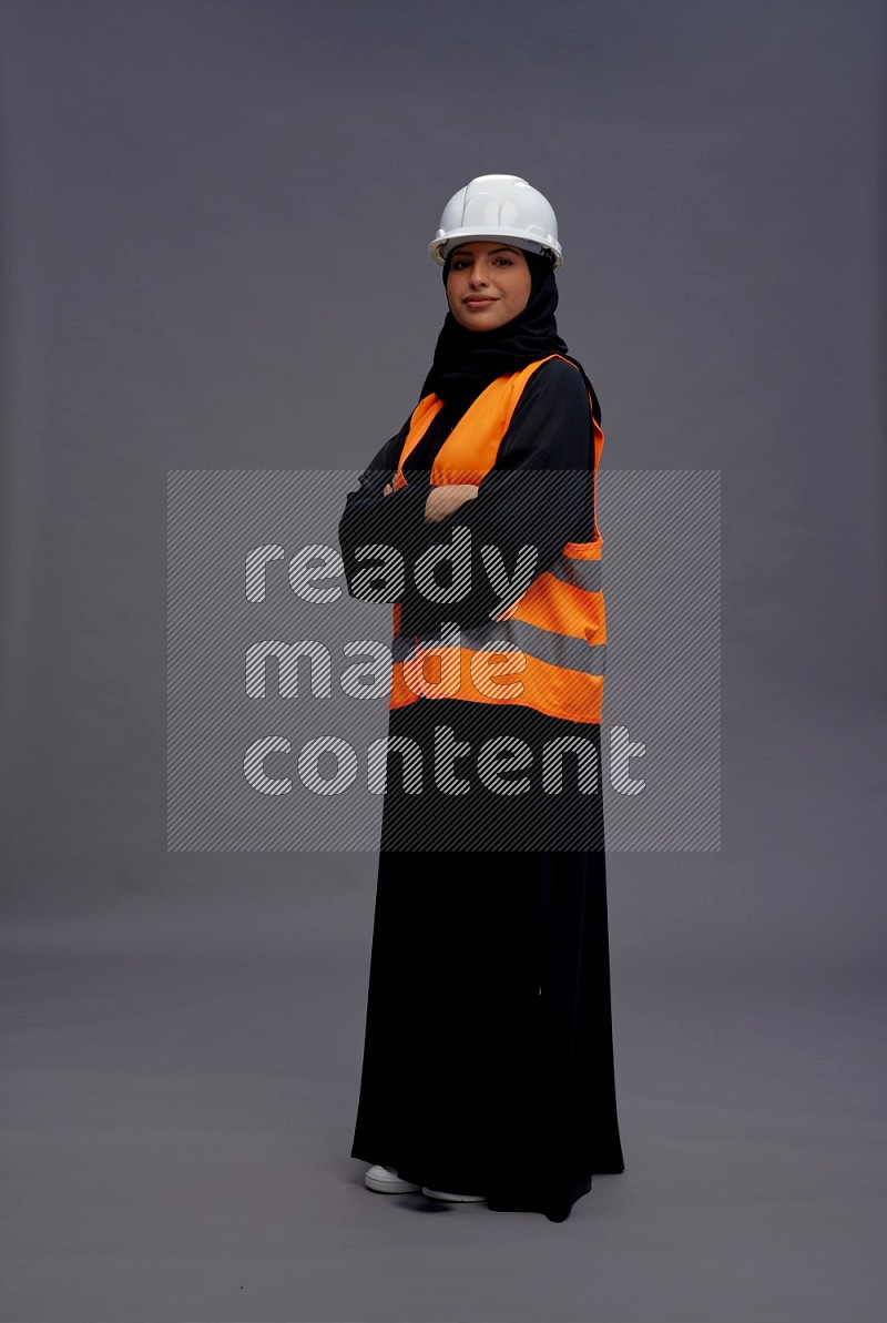Saudi woman wearing Abaya with engineer vest standing with crossed arms on gray background