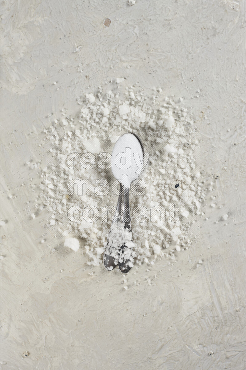 2 metal spoons filled with fine table salt and fine pink himalayan salt on white background