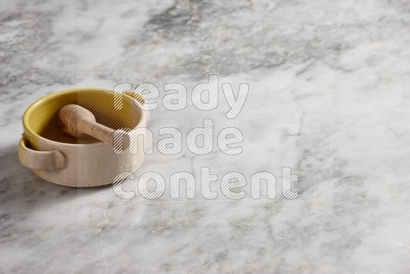 Multicolored pottery bowl with wooden honey dipper in it on grey marble background