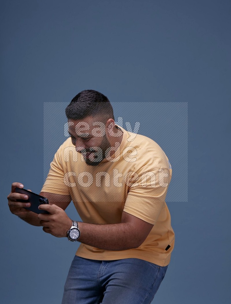A man Playing Games on Smartphone on Blue Background wearing Orange T-shirt