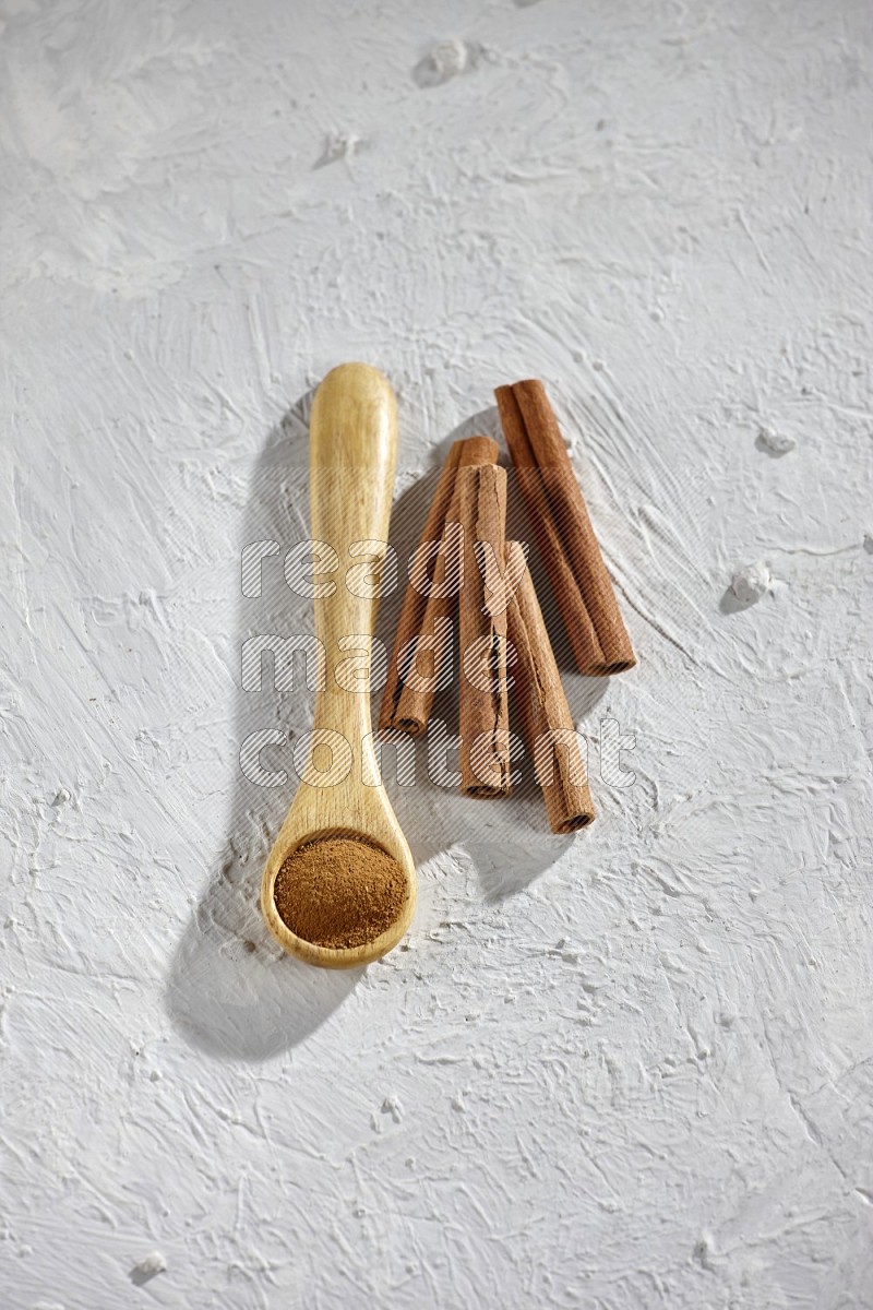 Cinnamon powder in a wooden spoon with cinnamon sticks on white background
