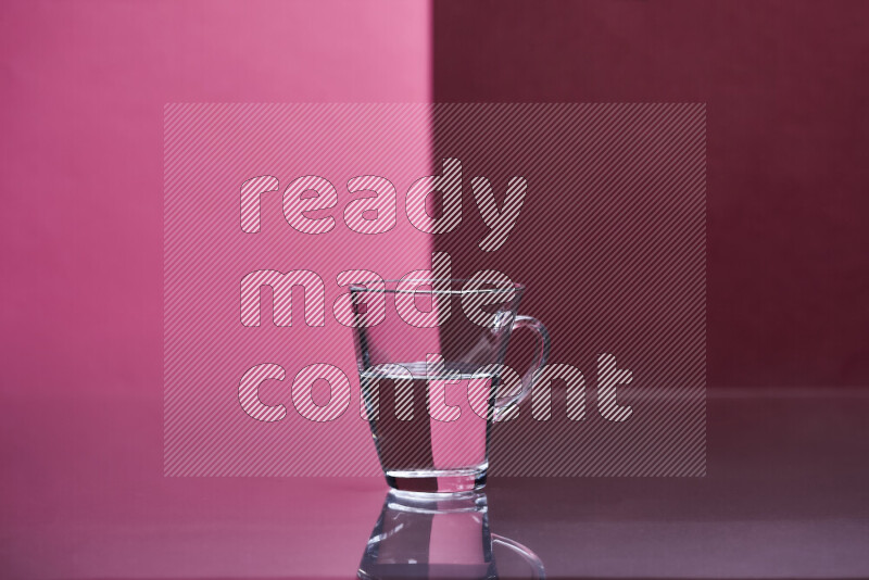 The image features a clear glassware filled with water, set against pink and dark red background