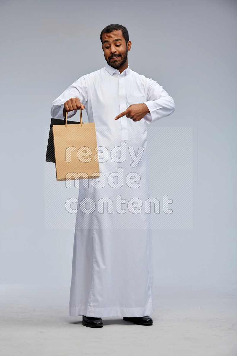 Saudi man Wearing thob standing holding shopping bag on Gray background