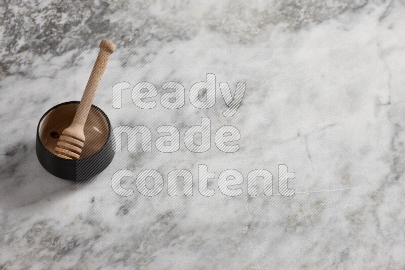 Black pottery bowl with wooden honey dipper in it on grey marble background