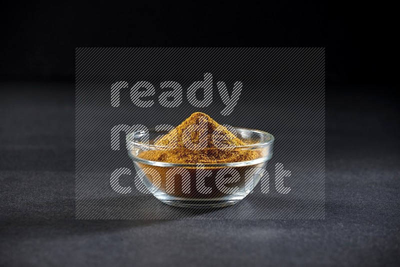 A glass bowl full of turmeric powder on black flooring