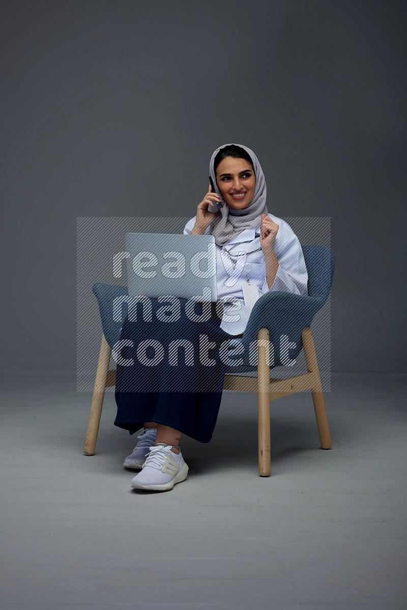 A doctor wearing a light gray head scarf sitting on blue chair on grey background