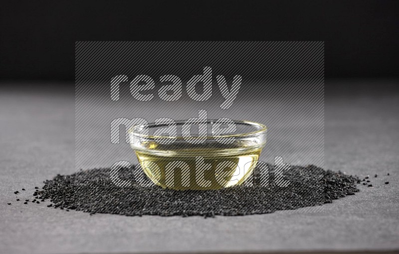 وعاء زجاجي ممتلئ بزيت حبة البركة محاط ببذور حبة البركة على أرضية سوداء
