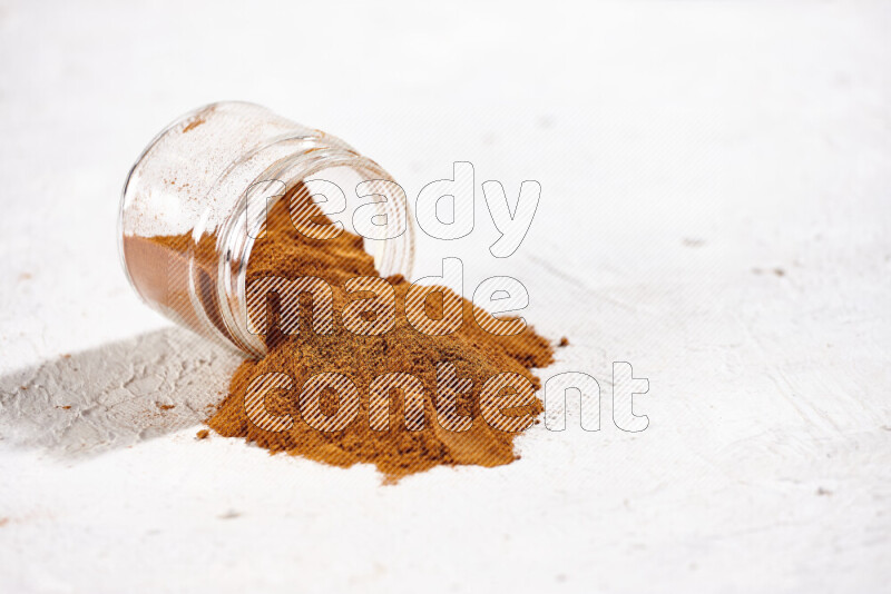 A glass jar full of ground paprika powder flipped with some spilling powder on white background