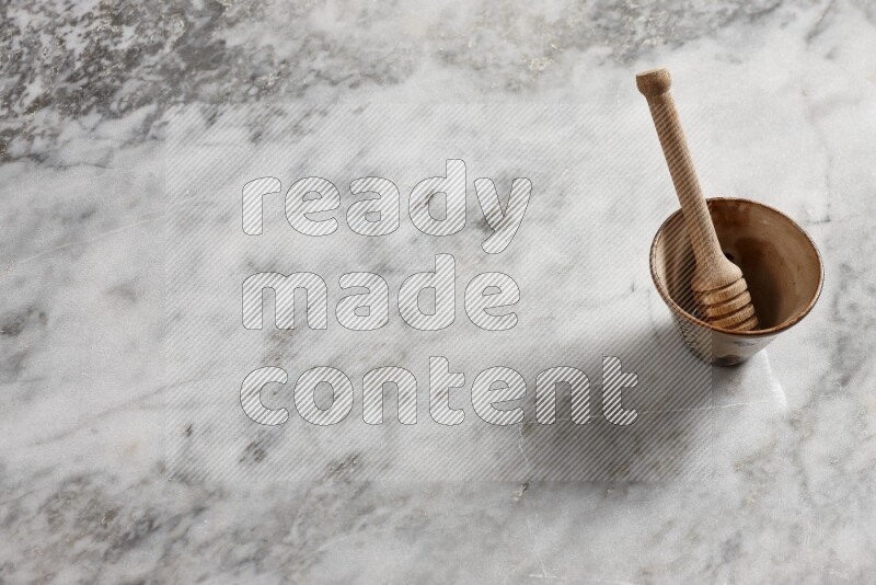 Decorative pottery bowl with wooden honey dipper in it on grey marble background