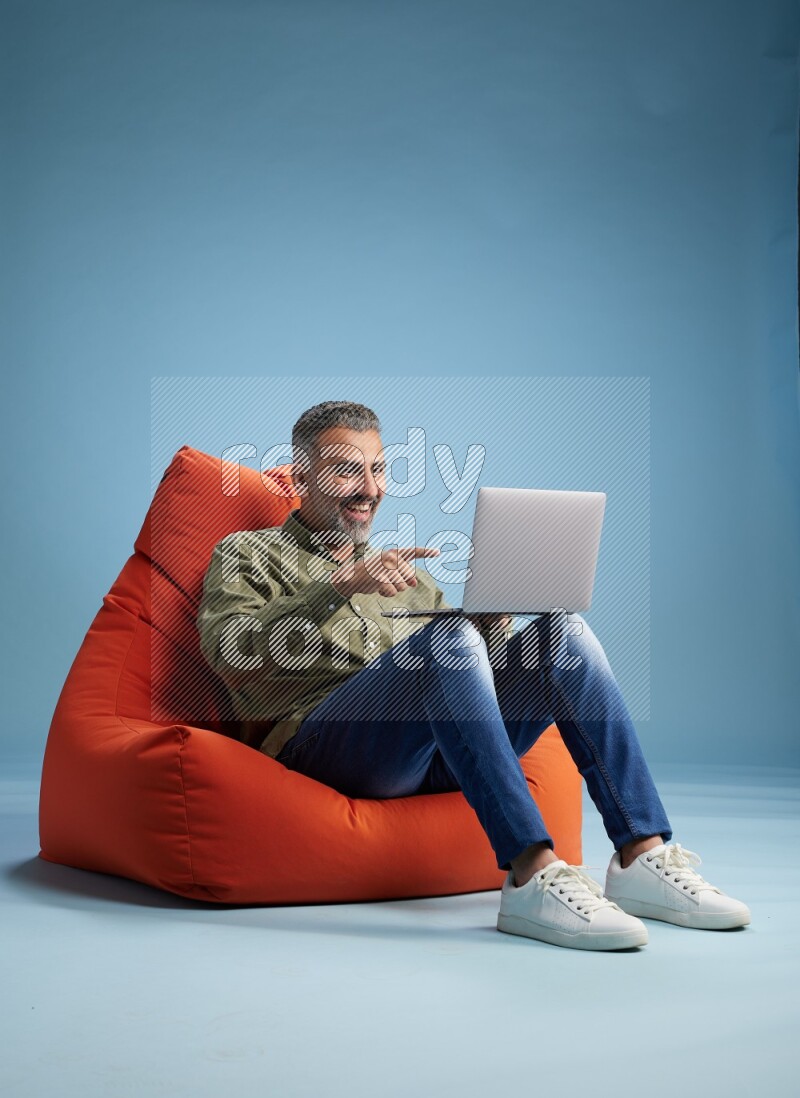 A man sitting on an orange beanbag and working on laptop