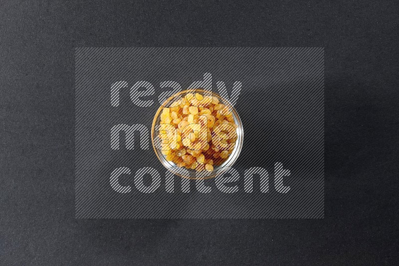 A glass bowl full of raisins on a black background in different angles