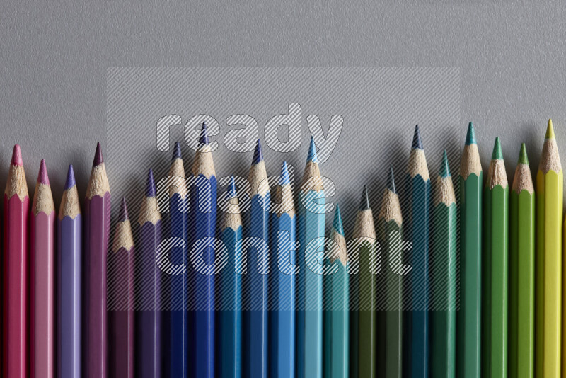 A collection of colored pencils arranged showcasing a gradient of different hues on grey background