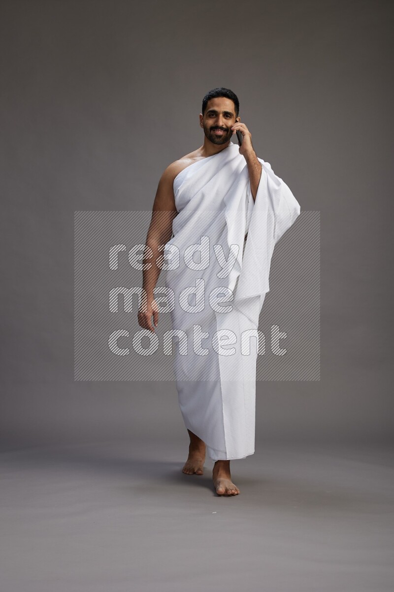 A man wearing Ehram Standing talking on phone on gray background