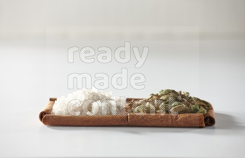 مربعان من أعواد القرفة ممتلئان بحبوب الهيل والملح الأبيض علي خلفية بيضاء