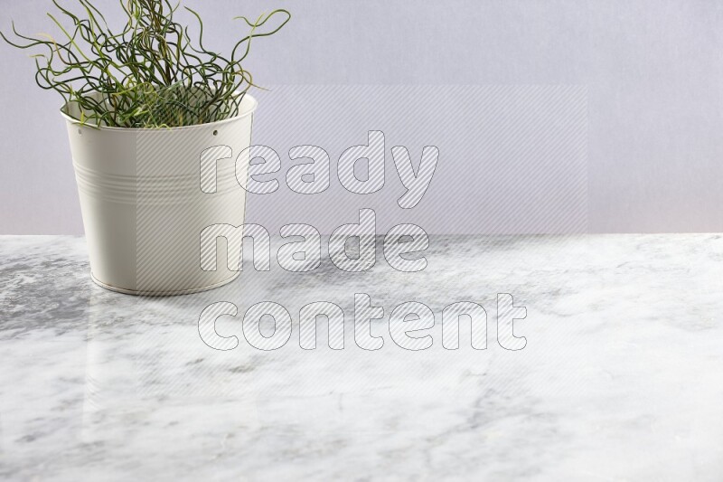 Green artificial plant in white pot on light grey marble background
