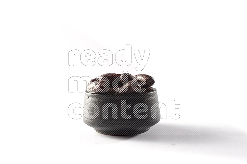 Dates in a black pottery bowl on white background