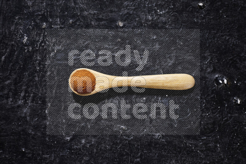 A wooden spoon full of ground paprika powder on black background