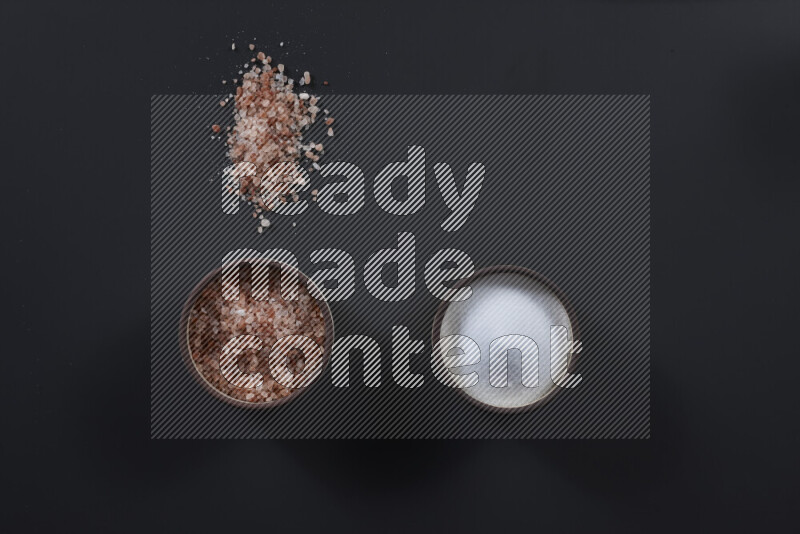 2 وعاء فخاري احدهمها ممتلئ بملح الهيمالايا والأخر بالملح الأبيض على خلفية سوداء