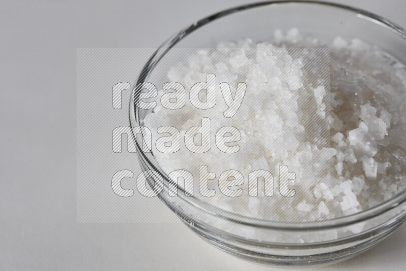 A glass bowl full of coarse sea salt crystals on white background