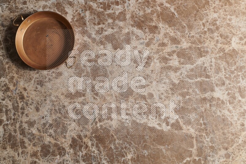 A small copper pan on beige marble background