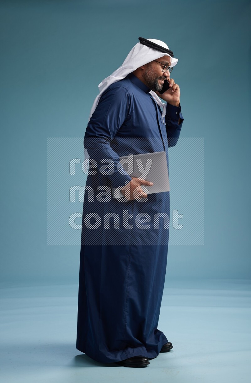 Saudi Man with shimag Standing talking on phone on blue background