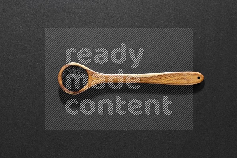 A wooden ladle full of black seeds on a black flooring