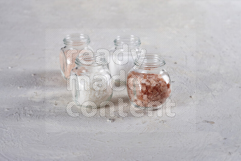 4 glass jars filled with table salt, coarse sea salt, fine himalayan salt and coarse himalayan salt on white background