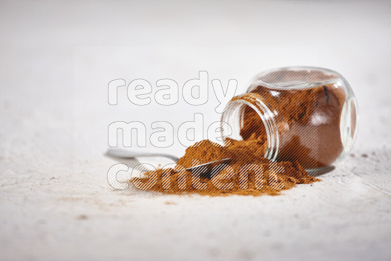 A glass jar full of ground paprika powder flipped with some spilling powder on white background