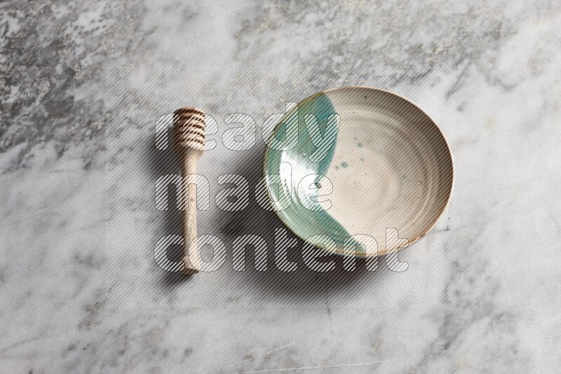 Multicolored pottery plate with wooden honey dipper on the side on grey marble background