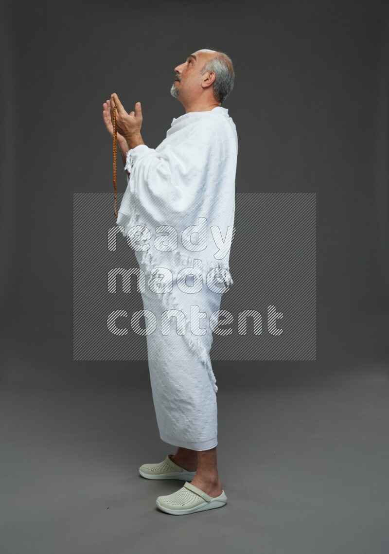 A man wearing Ehram Standing dua'a on gray background