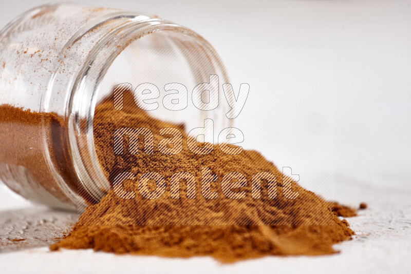 A glass jar full of ground paprika powder flipped with some spilling powder on white background