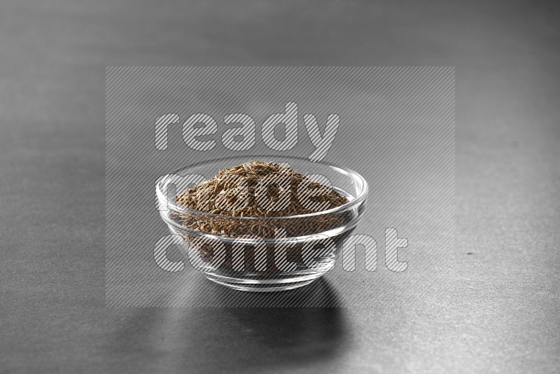 A glass bowl full of cumin on black flooring