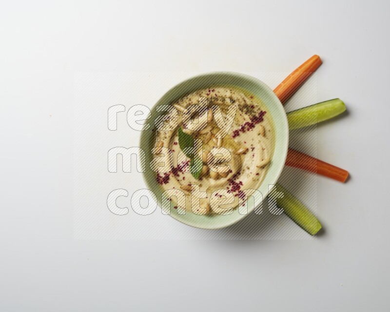 Hummus in a green plate garnished with zattar & sumak on a white background
