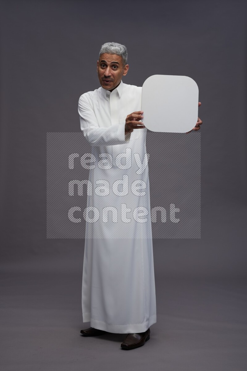 Saudi man wearing thob standing holding social media sign on gray background