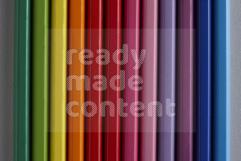 مجموعة من أقلام الرصاص الملونة مرتبة لتعرض تدرجا من الألوان المختلفة علي خلفية رمادية