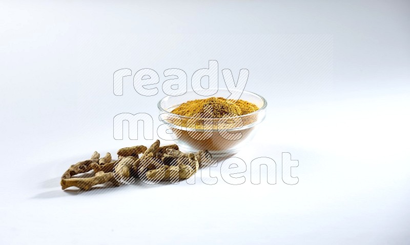 A glass bowl full of turmeric powder and dried whole fingers beneath it on white flooring