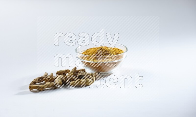 A glass bowl full of turmeric powder and dried whole fingers beneath it on white flooring