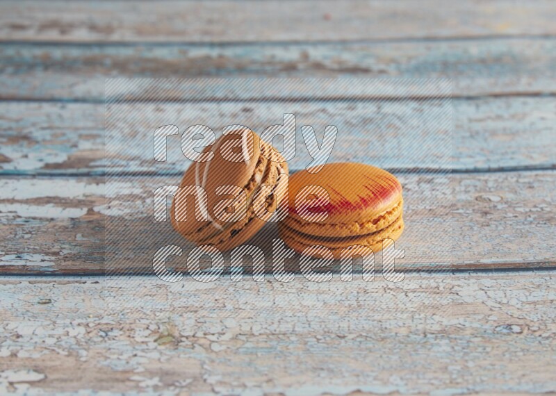 45º Shot of of two assorted Brown Irish Cream, and Orange Exotic macarons on light blue background