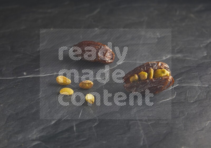 two pistachios stuffed madjoul dates on a black textured background