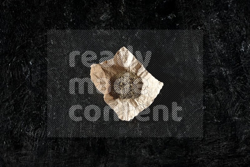 Cardamom powder in a crumpled piece of paper on textured black flooring