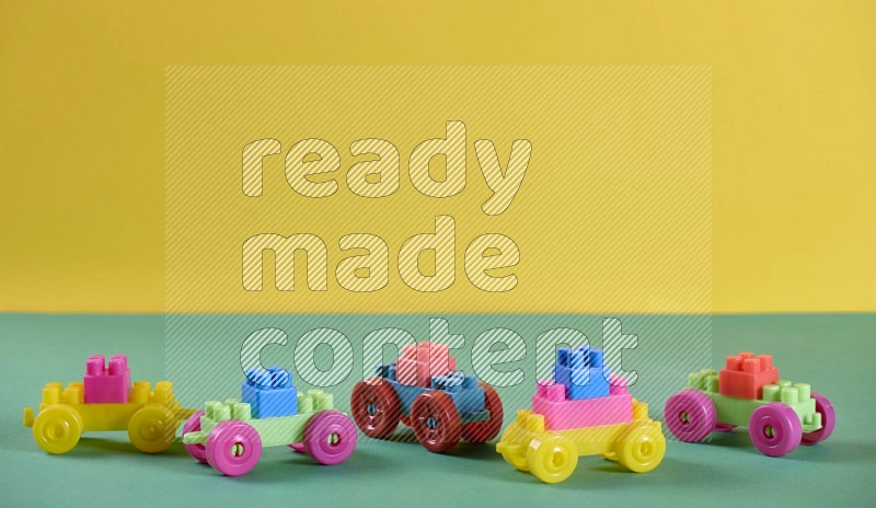 Plastic little cars and building blocks on yellow and green background in different angles (kids toys)