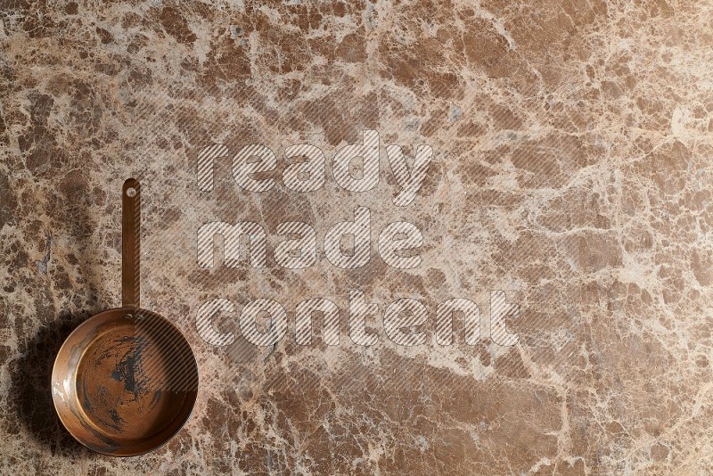 Top View Shot Of A Small Copper pan On beige Marble Flooring