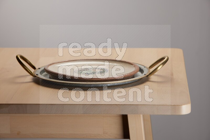 multicolored plate placed on a rounded stainless steel tray with golden handels on the edge of wooden table