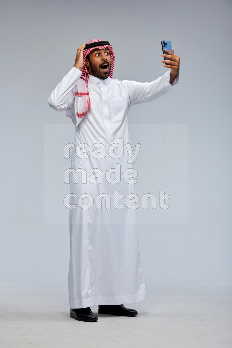 Saudi man Wearing Thob and shomag standing taking selfie on Gray background