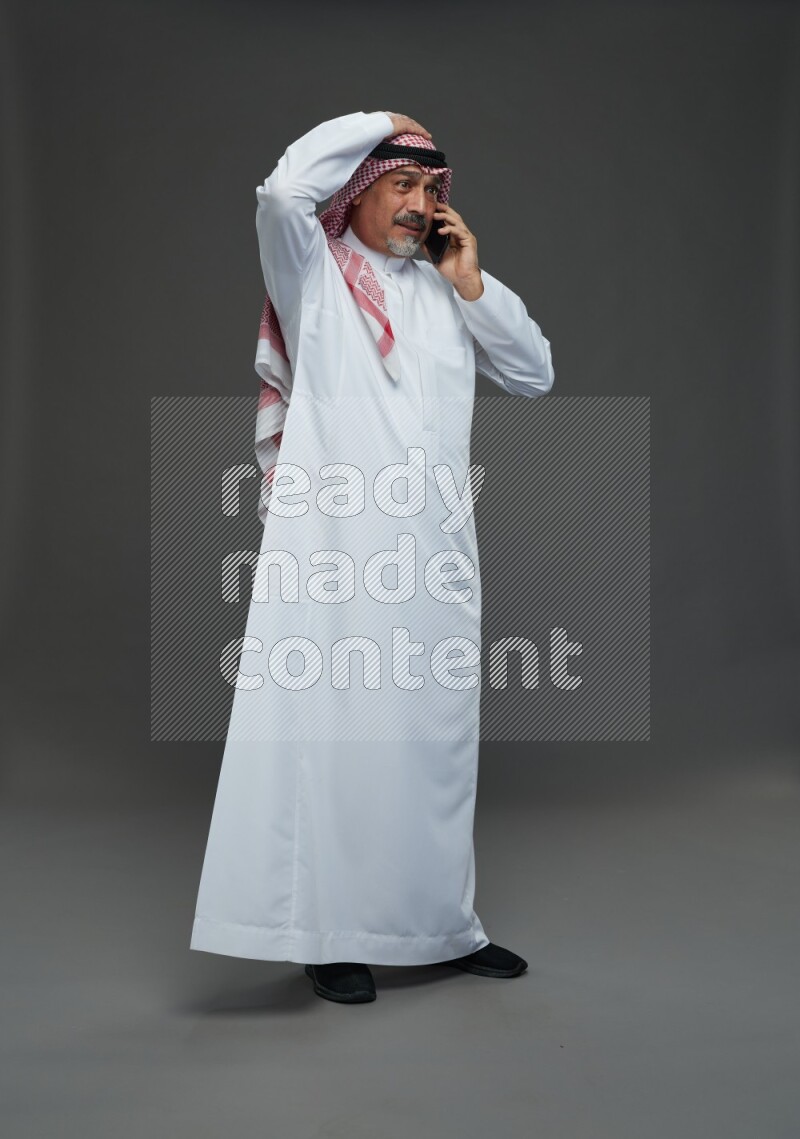 Saudi man with shomag Standing talking on phone on gray background