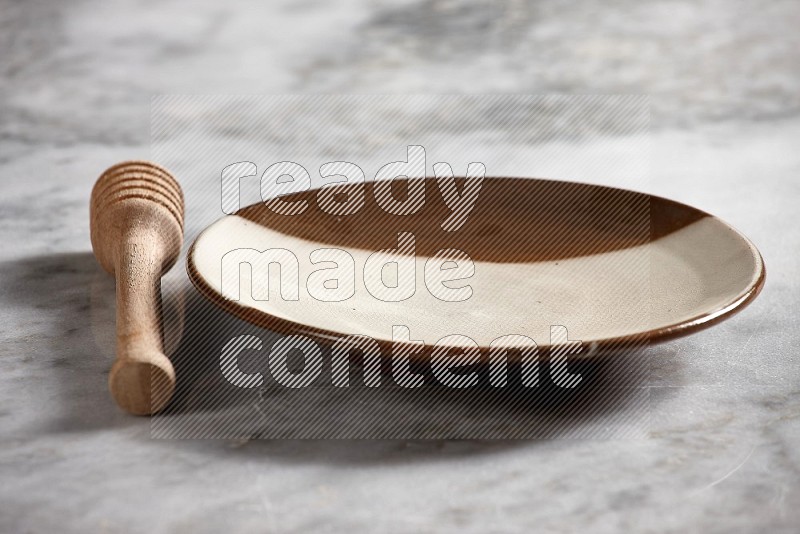 Multicolored Pottery Plate with wooden honey handle on the side with grey marble flooring, 15 degree angle