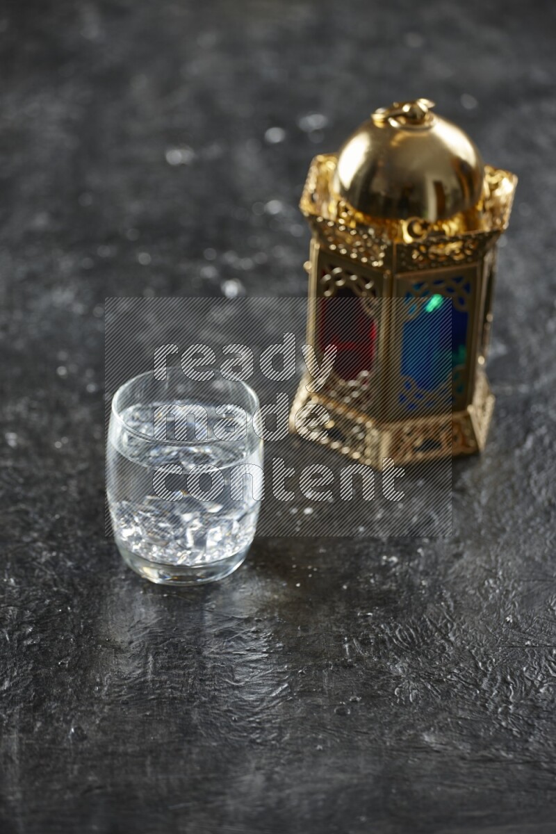 A golden lantern with different drinks, dates, nuts, prayer beads and quran on textured black background