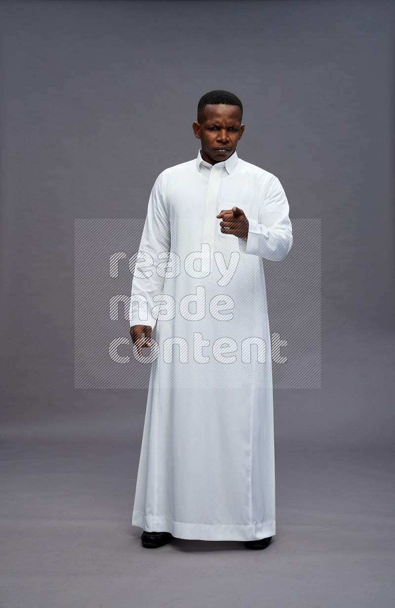 Saudi man wearing thob standing interacting with the camera on gray background