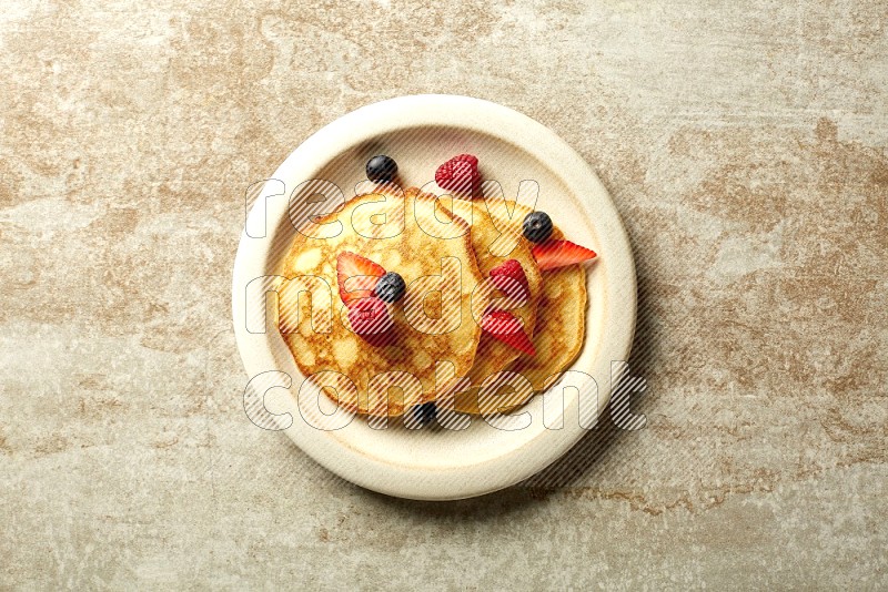 Three stacked mixed berries pancakes in a beige plate on beige background